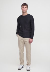 Black long-sleeve textured sweater with a round neck, paired with beige chinos and black-and-white sneakers.