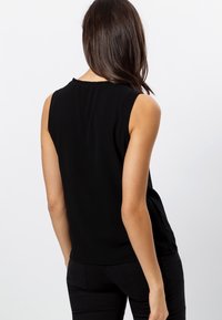 Blusa sin mangas negra con cuello redondo, textura de tela suave y un sutil detalle fruncido en la parte posterior del escote.