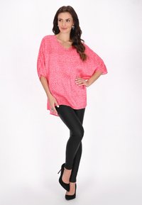 Bluză oversized cu imprimare leopard roz, cu decolteu în V, mâneci scurte și tiv înalt-jos, asortată cu pantaloni negri mulați și tocuri negre.