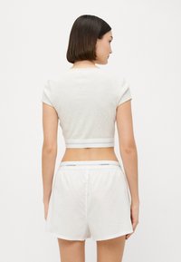 Grå kort topp med korta ärmar, parat med vita shorts. Toppen har en platt midja med ljusgrå ränder och en logotyp på midjan.