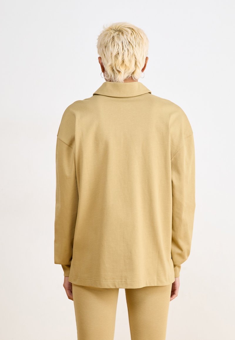 Chemise oversize beige en tissu doux, dotée d'un col classique et de manches longues, avec une coupe décontractée et une texture subtile.