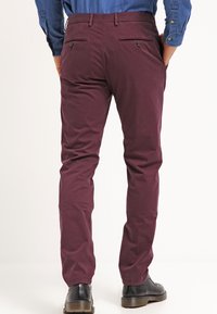 Pantaloni color bordeaux realizzati in cotone testurizzato, con tasche posteriori e chiusura con bottone, caratterizzati da una vestibilità slim e un design a gamba affusolata.