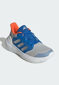 Chaussure de sport grise avec des accents bleus, tige en maille texturée, col rembourré orange, semelle blanche, et trois rayures grises sur le côté.