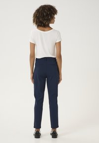 Haut blanc à manches courtes associé à un pantalon taille haute navy. Le pantalon possède des poches arrière et se resserre légèrement à la cheville. Chaussures noires incluses.