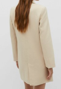 Beige uld-blandingsfrakke med lange ærmer, lige snit og en enkelt baglomme. Glat tekstur; enkel, uudsmykket design.
