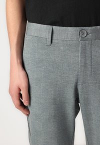 Gray checkered trousers with a smooth texture, featuring a button closure and subtle red accents in the pattern, tailored fit, and belt loops.