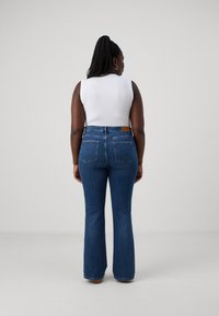Vaqueros acampanados de color azul oscuro con una textura de denim suave, que presentan una cintura alta, dos bolsillos traseros y una etiqueta de cuero marrón en la cinturilla.