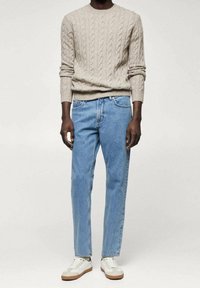 Suéter beige de punto con cable combinado con vaqueros azul claro y zapatillas blancas casuales con detalles marrones y suelas texturizadas.