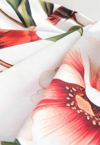 Kukkakuvioinen kangas, jossa on kirkas punaisia ja oransseja kukkia valkoisella taustalla, pehmeä tekstuuri ja hienostuneet detaljit terälehdissä.