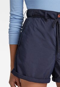 Námořnické modré šortky s elastickým pasem na šňůrku, ohrnutými lemy a bočními kapsami; vyrobené z lehkého materiálu s hladkou texturou.
