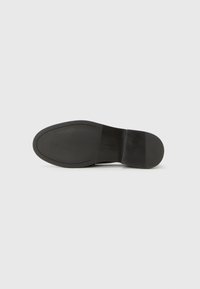 Schwarze Schuhsohle mit glatter Oberfläche, runder Form und dezenten Profilmustern, mit eingeprägtem Markenlogo in der Nähe der Ferse.