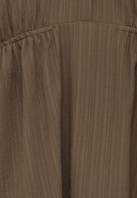 Tissu marron froissé avec une texture verticale et un détail de couture froncée, créant un effet légèrement plissé.