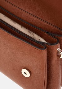 Braune Lederhandtasche mit strukturiertem Oberflächen, einem goldenen Druckverschluss und einem beigen Innenraum mit gedrucktem Branding. Zwei sichtbare Fächer.