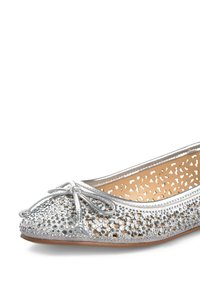 Scarpa piatta argento con punta rotonda, decorata con rhinestone su una superficie perforata, e un fiocco decorativo sul davanti. Suola liscia.