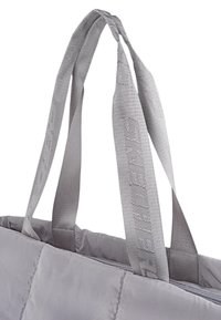 Bolso tote gris acolchado con dos asas texturizadas grises, que presenta un sutil patrón de logo a lo largo de la correa. Cierre superior con cremallera.