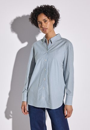Camicia a righe blu e bianche con bottoni, maniche lunghe, colletto e tasca; abbinata a jeans blu scuro. Tessuto morbido, vestibilità normale.