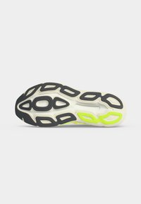 Semelle de chaussure de sport blanche avec des crampons en caoutchouc noirs et jaune néon conçus pour la traction et l'amorti.