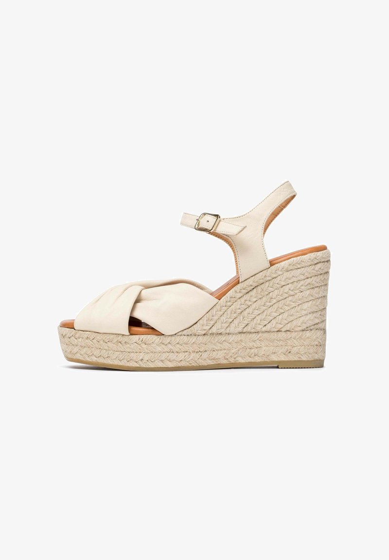 Sandalia de cuña beige con una tira de tela retorcida, punta abierta y correa ajustable en el tobillo. Presenta una suela de yute trenzado para agregar textura.
