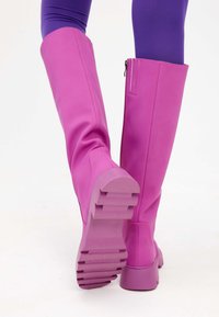 Roze kniehoge laarzen van soepel synthetisch materiaal, met een zware zool en een rits aan de zijkant. Gelaagd profiel voor grip.