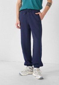 Marineblauwe sweatpants met een elastische tailleband en trekkoord, voorzien van zijzakken en ribgebreide manchetten. Zachte stoftextuur.