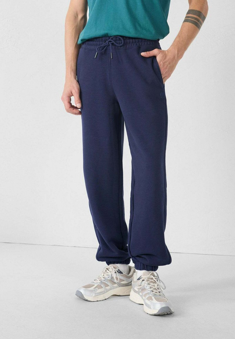 Marineblauwe sweatpants met een elastische tailleband en trekkoord, voorzien van zijzakken en ribgebreide manchetten. Zachte stoftextuur.