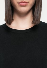 Czarny sweter z dzianiny z okrągłym dekoltem i gładką teksturą, z widocznymi prążkami wzdłuż kołnierza. Zbliżenie na górną część torsu.