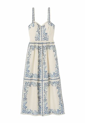 Mujer con un vestido midi crema con patrones florales azules, sosteniendo un bolso azul tejido y llevando sandalias marrones con plataforma.