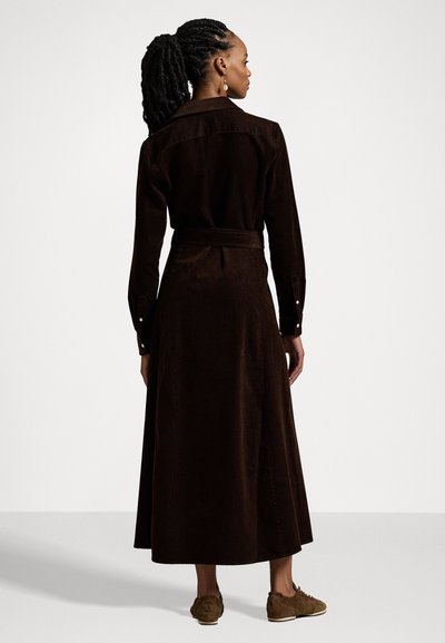 Brun kordfløjlskjole med krave, lange ærmer og bindebælte, der har maxilængde og sideslit langs kanten for bevægelsesfrihed.