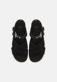 Paire de sandales en daim noir avec des brides croisées et des boucles réglables à la cheville, présentées vues de dessus sur un fond uni.