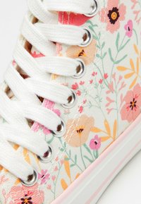 Tenis din pânză cu un model floral alb, având flori roz, portocalii și mov, șireturi albe și gauri metalice argintii. Toc din cauciuc roz.