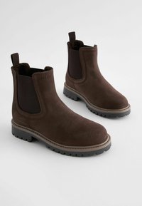 Bottines en daim marron avec des panneaux élastiques sur les côtés, semelles en caoutchouc crantées et tirants pour un enfilage facile. Fini texturé avec des accents cousus.