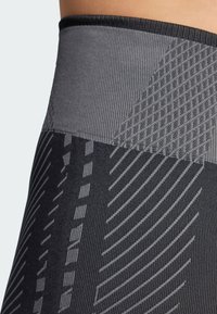 Leggings sportivi neri con una cintura grigia testurizzata e accenti dinamici a motivo in diverse tonalità di grigio, che enfatizzano un design elegante.
