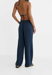 Marineblauwe, loszittende broek van textuurstof. Kenmerkt zich door een wijd beenontwerp met een elastische tailleband en een lichte draping.