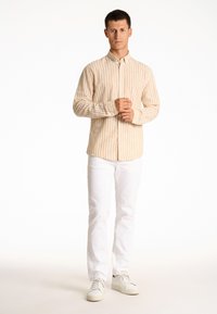 Lichtbeige overhemd met verticale strepen, lange mouwen en een standaard kraag, gecombineerd met witte jeans en witte sneakers.