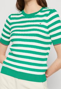 Top a maniche corte a righe verdi e bianche in maglia con tessuto a coste, scollatura rotonda e piccolo logo sul petto.