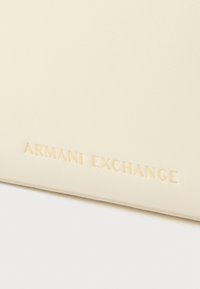 Krémová peněženka z faux kůže s vyraženým logem "ARMANI EXCHANGE". Hladký povrch, obdélníkový tvar, minimalistický design, žádný výrazný hardware.