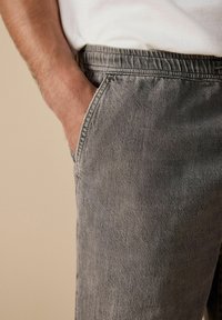 Pantaloni din denim gri, cu o croială relaxată, având talie elastică și buzunare laterale, prezentând o suprafață moale, texturată.