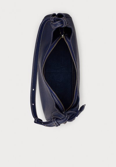 Temno modra usnjena torbica z teksturirano površino, zadrgo za zapiranje in vozlom okrašenim ročajem. Notranjost je obložena s temno tkanino.