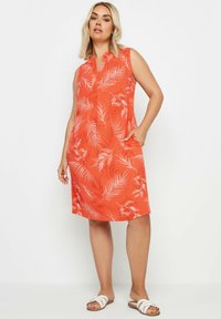 Ärmlängdlös orange klänning med bladmönster, detalj vid kragen, sidofickor och en avslappnad passform. Bärs med vita sandaler.