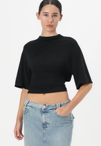 Zwarte cropped top met een hoge hals en korte mouwen, gecombineerd met een lichtblauwe denim rok. Glad materiaal, aansluitend ontwerp.