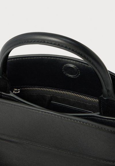 Czarna skórzana torba typu tote z krótkimi uchwytami, z otwartym górnym otworem, wewnętrzną kieszenią na suwak i tekstylną podszewką. Gładka faktura i minimalistyczny design.