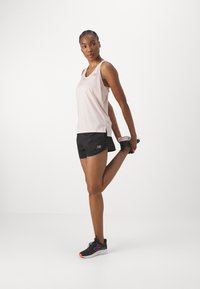 Light pink tank top with a logo, paired with black shorts. She is stretching while wearing black athletic shoes with purple accents.