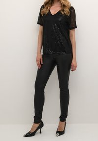 Svart paljett-topp med korta ärmar och V-ringning, matchad med figurnära svarta byxor i konstläder och svarta klackskor med spetsig tå och metalliska detaljer.