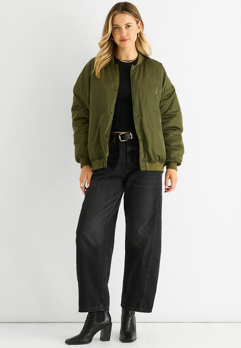 Olive green bomber jacket with a smooth, matte finish, snap buttons, and ribbed cuffs, paired with high-waisted black jeans and ankle boots.
