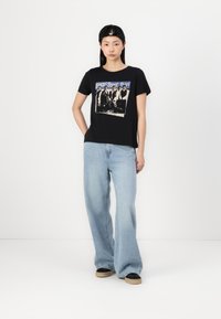 T-shirt noir à manches courtes avec un graphisme vintage des Backstreet Boys. Associé à un jean en denim clair à jambes larges et des baskets noires.
