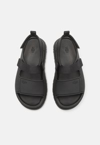 Sorte sandaler med en teksturert gummisåle, justerbare stoffremmer og logoaccent. Åpen tå-design med en polstret fotbed.