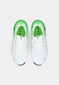 White athletic shoes with green accents, textured upper, lace closure, and black sole. Features branding on the side and heel.