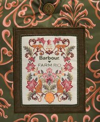 Grüner Stoff mit rosa und orangefarbenen Blumenmustern zeigt ein cremefarbenes rechteckiges Etikett. Das Etikett zeigt gestickte Leoparden und Blumendesigns.
