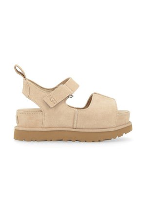 Sandalias de ante beige con una correa ancha, cierre ajustable de gancho y bucle, y una suela de goma gruesa y texturizada. Incluye una pestaña trasera para tirar.