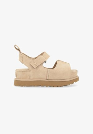 Sandalias de ante beige con una correa ancha, cierre ajustable de gancho y bucle, y una suela de goma gruesa y texturizada. Incluye una pestaña trasera para tirar.